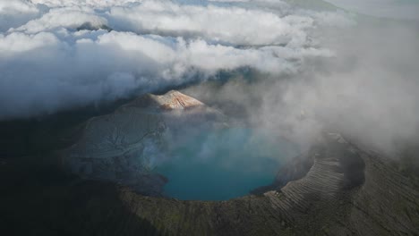 panoramic view of ijen volcano with turquoise sulfur lake, clouds rolling in over mountains