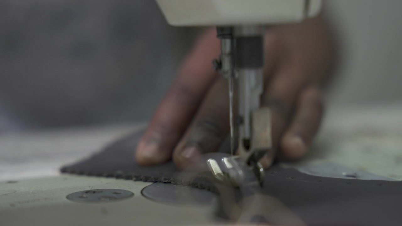 Une aiguille de machine à coudre traverse le cuir tandis que des mains guident le matériau. Illustre le processus complexe de confection de vêtements. Utile pour le contenu de l'industrie de la mode