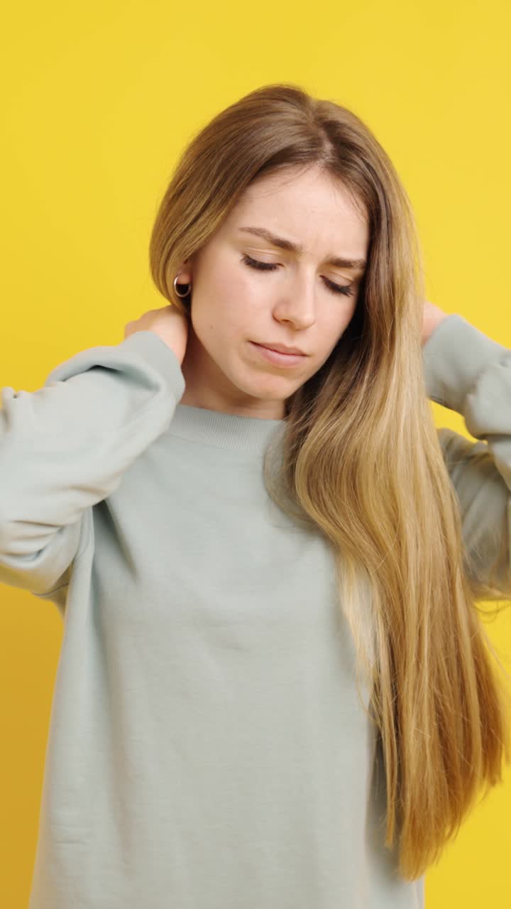 Young woman massaging neck on yellow background