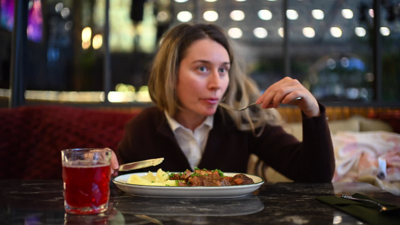 Woman eating mashed potatoes and meat at a restaurant table using fork and knife