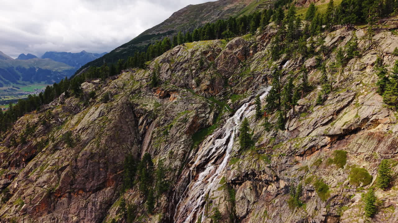 Lateral drone pan revealing rocky alpine waterfall and distant Swiss valley