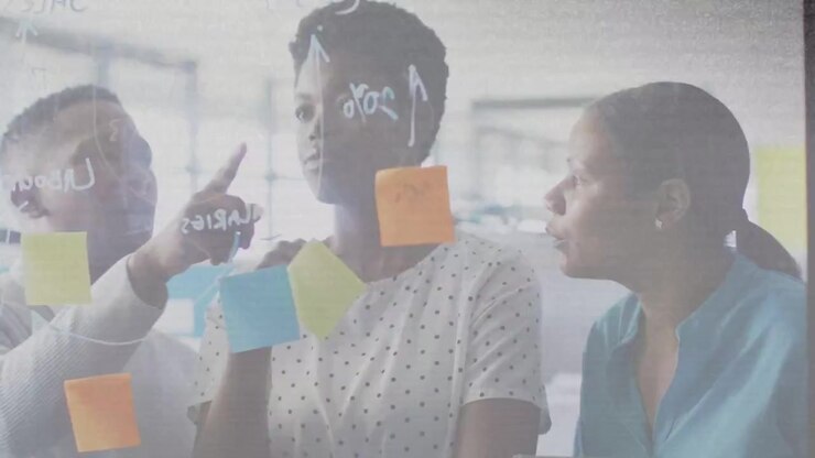 Center woman holding marker behind glass left peer nudging blue note team aligning business ideas