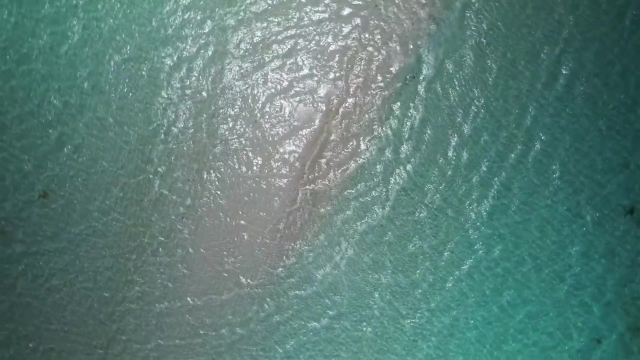 Mesmerizing overhead perspective revealing clear tropical waves rippling gently across a white submerged shore.
