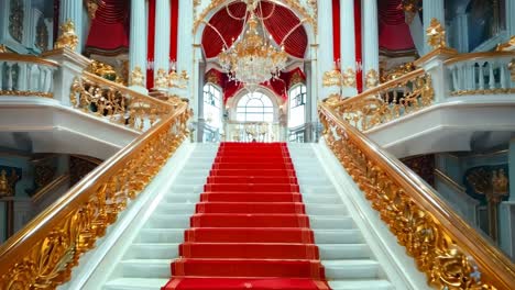 a red carpeted staircase in a building with a chandelier and chandeliers