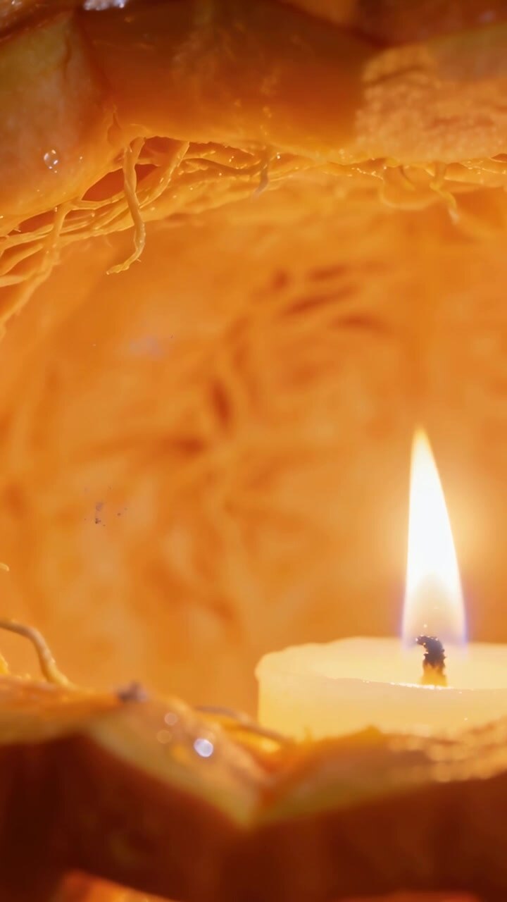 Vertical video: Flickering tealight burning inside gourd, lighting inner strands and melting wax