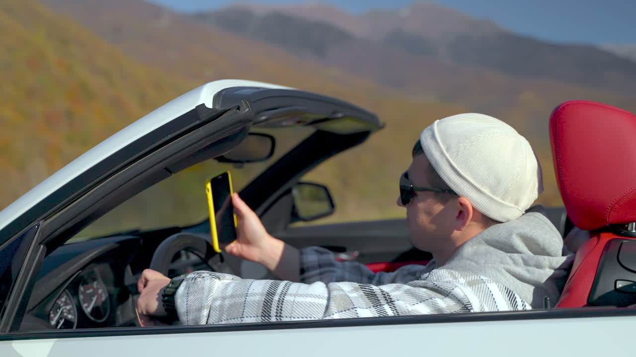 경치 좋은 산길에서 컨버터블 자동차에서 셀피를 찍는 남자