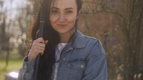 Vista-Cercana-De-Una-Mujer-Caucásica-Sosteniendo-Un-Rastrillo-Y-Sonriendo-A-La-Cámara-En-El-Campo