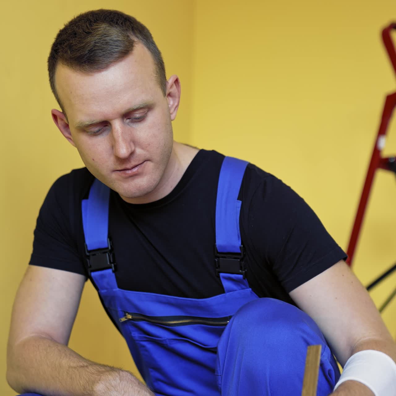 Portret van een werker die verf voorbereidt voor renovatie. Vakman in blauwe overall mengt verf op de achtergrond van een ladder in de kamer