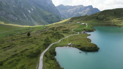 Push-in:-Drohnen-Luftaufnahme-Des-Ufers-Eines-Alpensees-Und-Ein-Gewundener-Pfad,-Auf-Dem-Die-Menschen-Die-Aussicht-Bewundern-Können,-Felsige-Berge-Im-Hintergrund,-Obwalden,-Engelberg