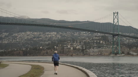 wide panning shot of running man in stanley park with lions gate bridge in back