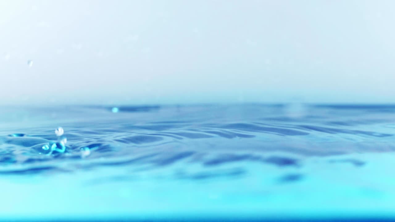 슬로우 모션의 깨끗한 물 표면은 물이 튀는 상점으로 화면을 채우고 기포로 액체 표면을 흔들고 있습니다.