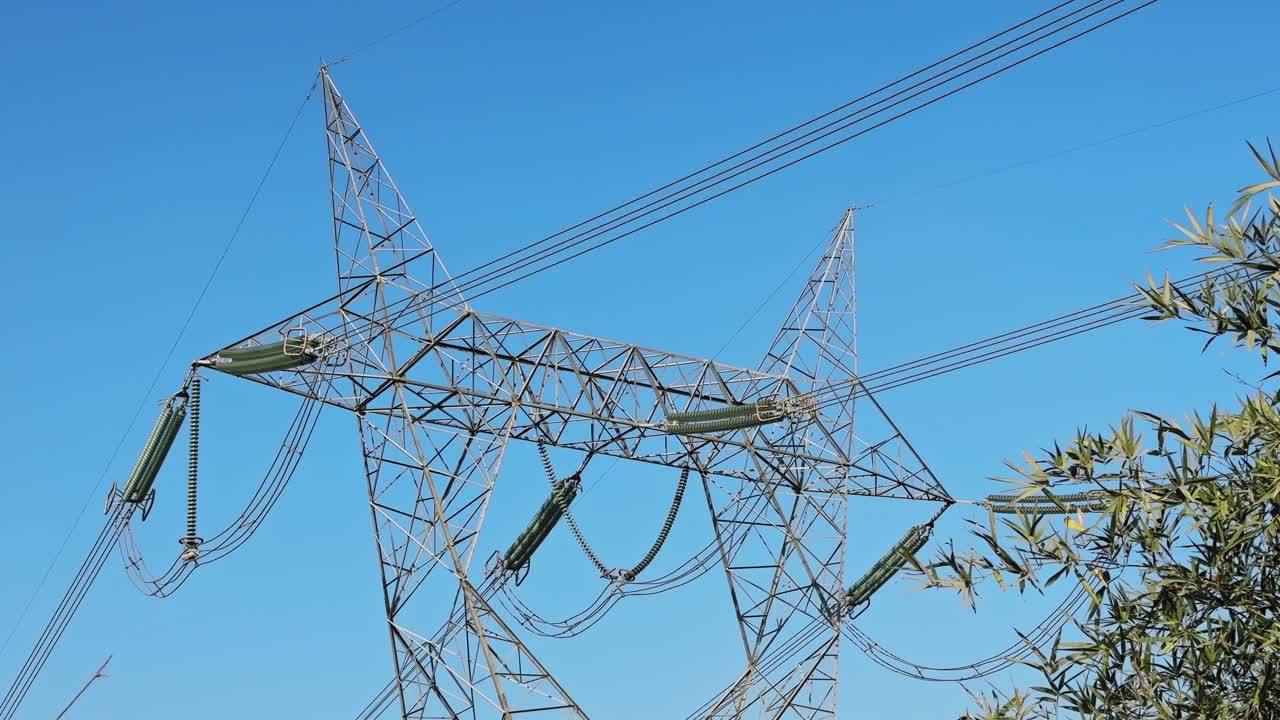 Static wide view of a steel lattice transmission tower with multiple insulator strings and overhead power lines stretching across a clear blue sky