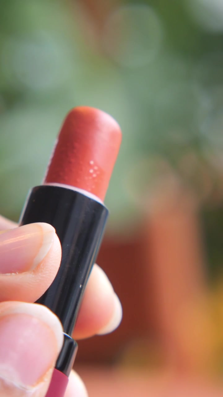 Hand Holding and Opening a Tube of Coral Lipstick