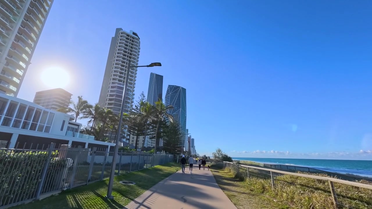 Vidvinkelbillede af folk, der går langs en solrig kyststi i Surfers Paradise, Australien.
