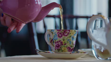 una toma apretada de una tetera rosa vertiendo té en una taza floral