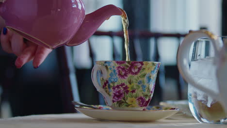 tight shot of a pink tea pot pouring tea into a floral cup