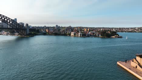 Aerial-View-Panning-From-Australian-Landmark-The-Sydney-Opera-House-To-Sydney-Harbour-Bridge-Behind-At-Sunset