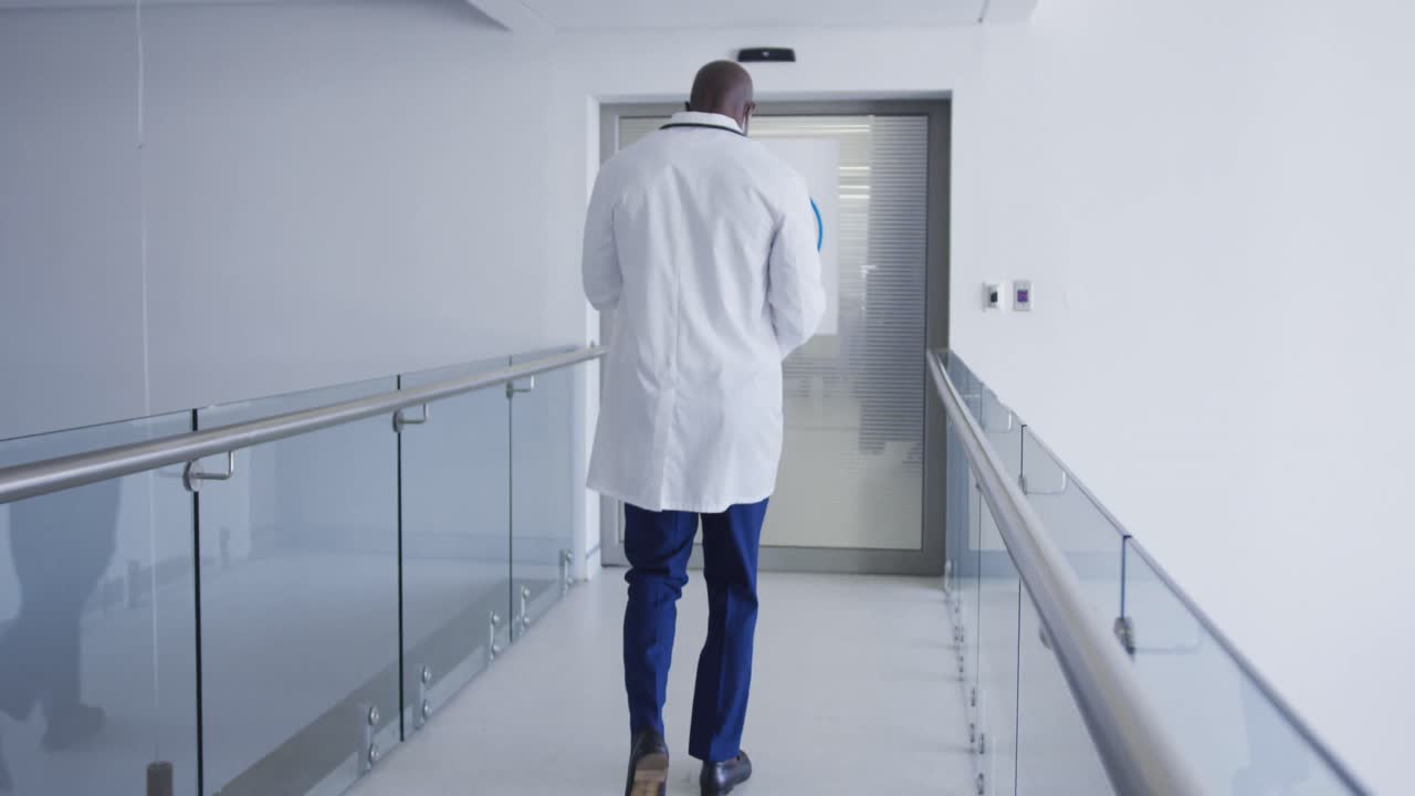 Médico afro-americano de costas caminhando pelo corredor do hospital.