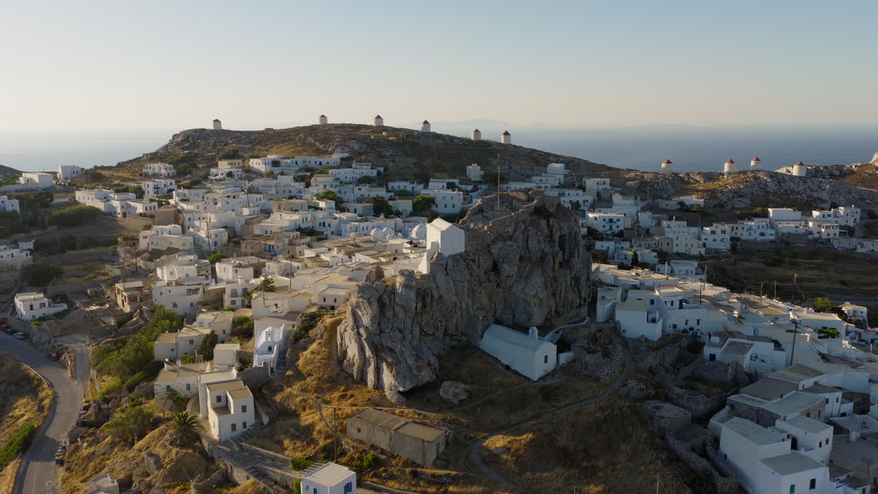 Aerial orbit around the medieval Castle of Amorgos in Chora during sunrise. The iconic Cycladic windmills create a timeless island backdrop