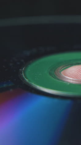 modern shining compact disk on young person finger with grooves on blurred dark background extreme close view