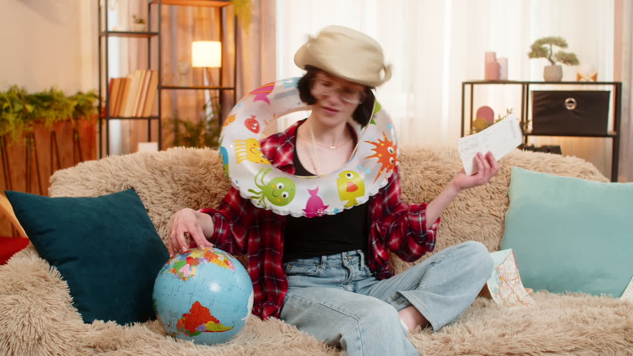 Woman planning beach vacation at home with inflatable swim ring holding globe and airplane tickets