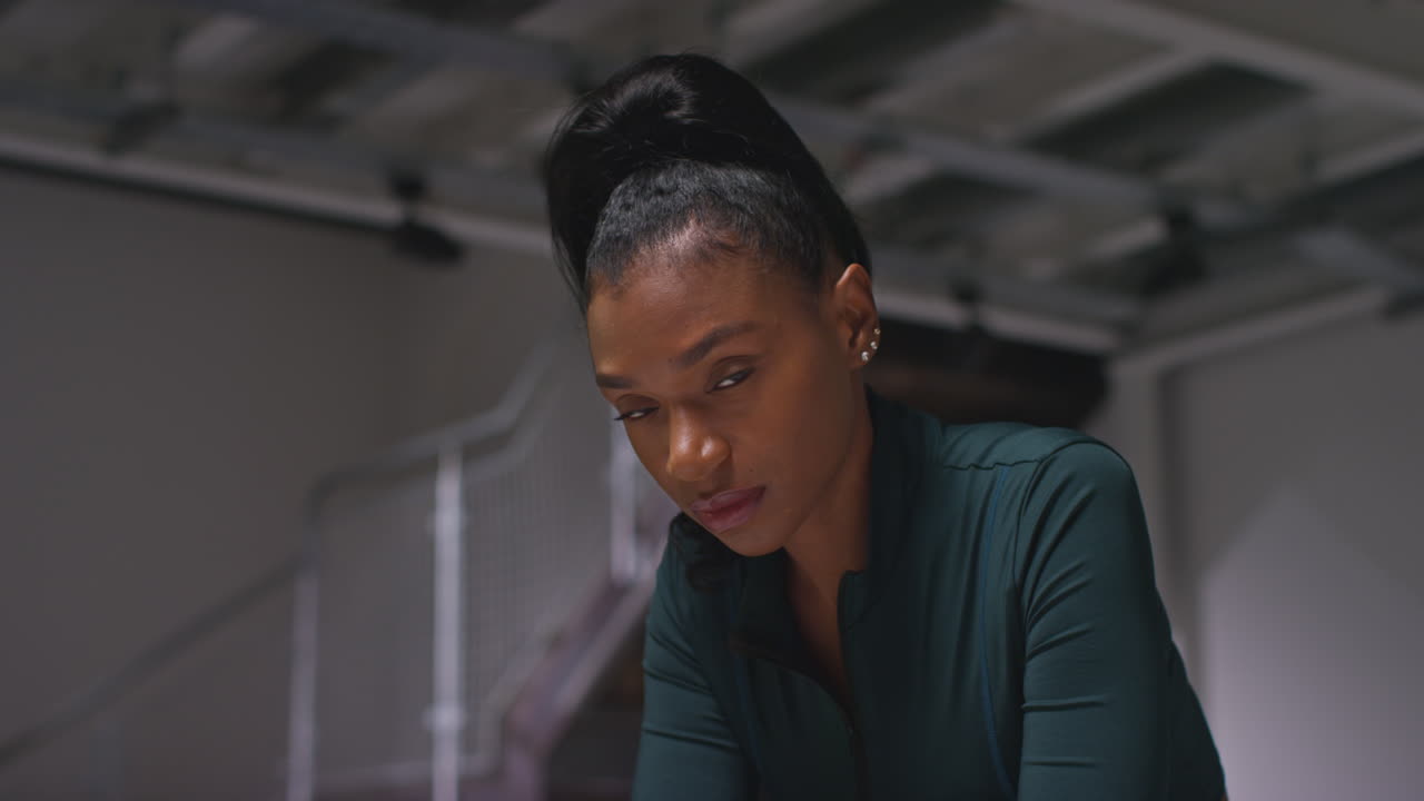 retrato de una atleta decidida entrenando en el gimnasio sentada y concentrada en el vestuario con una expresión enfocada 1
