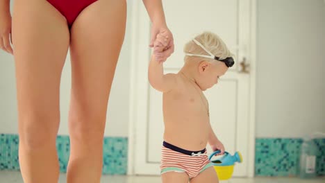 young mother and her cute little blonde child walking near swimming pool. happy mom spending time playing with her baby before the swimming lesson. happy healthy family together