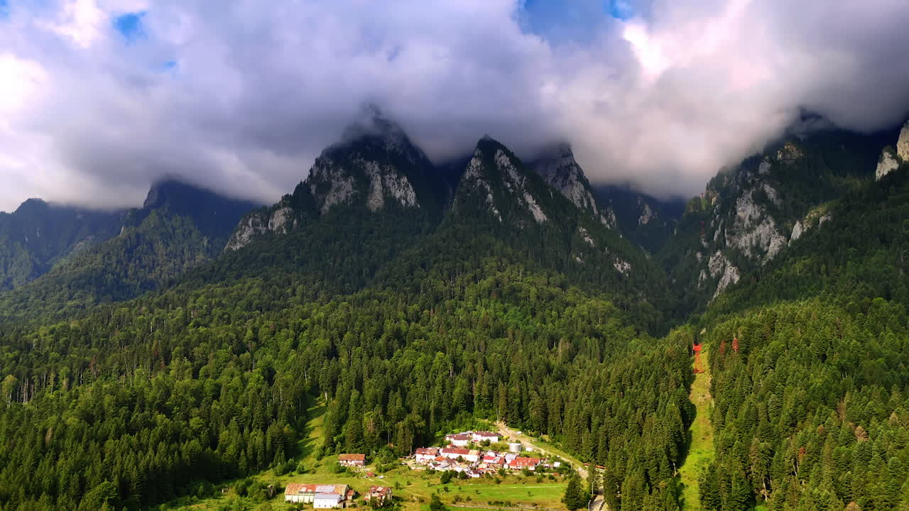Uno spesso e soffice paesaggio di nuvole copre le cime delle montagne. Un bosco di pini ricopre i pendii e circonda il villaggio. Carpazi meridionali, Romania