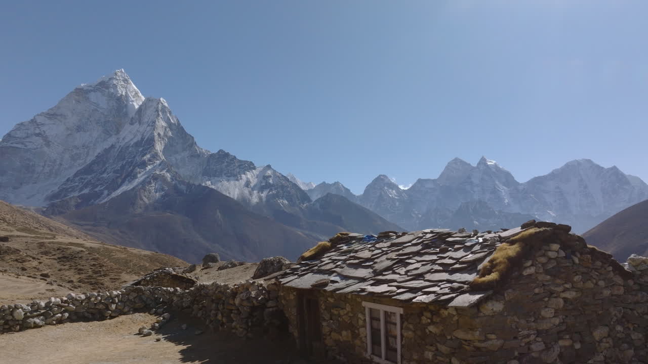 An orbiting pull-in drone shot passes a Himalayan rural house, then reveals a glacier river and snow-capped Ama Dablam mountains in Everest region Nepal