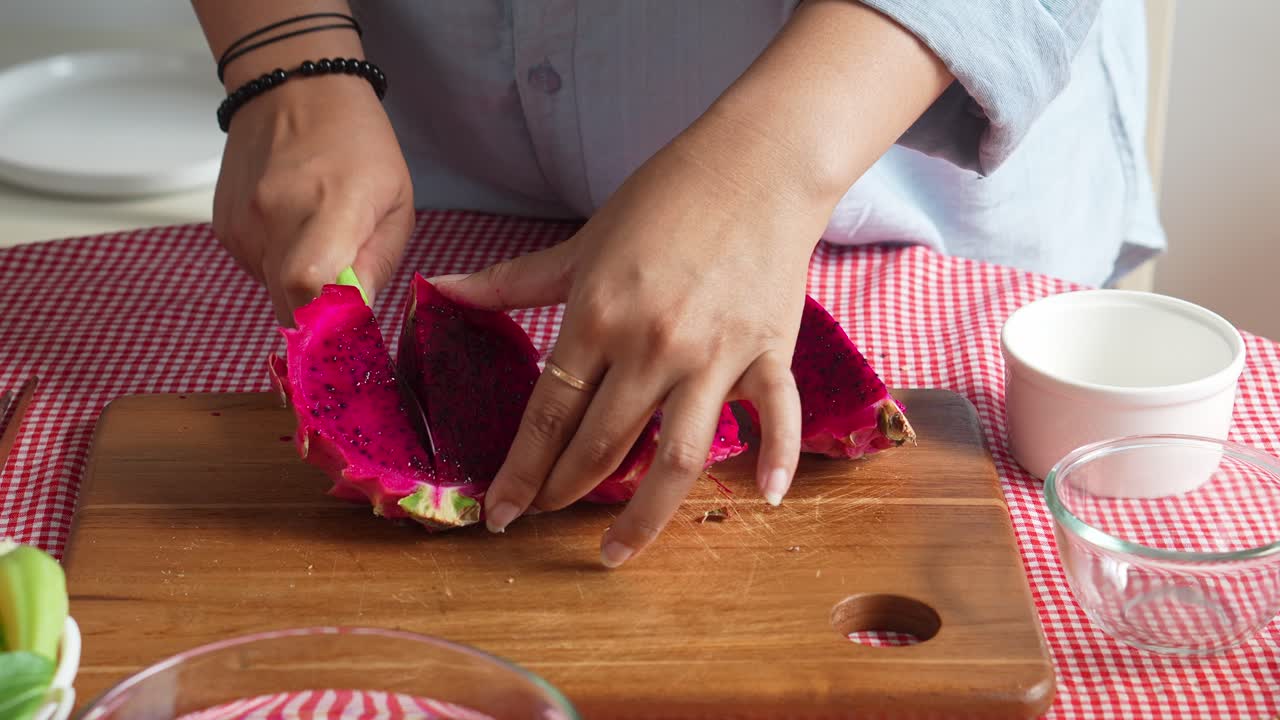 manos de mujer cortando frutas de dragón con un cuchillo en una tabla de madera para preparar jugo saludable en casa