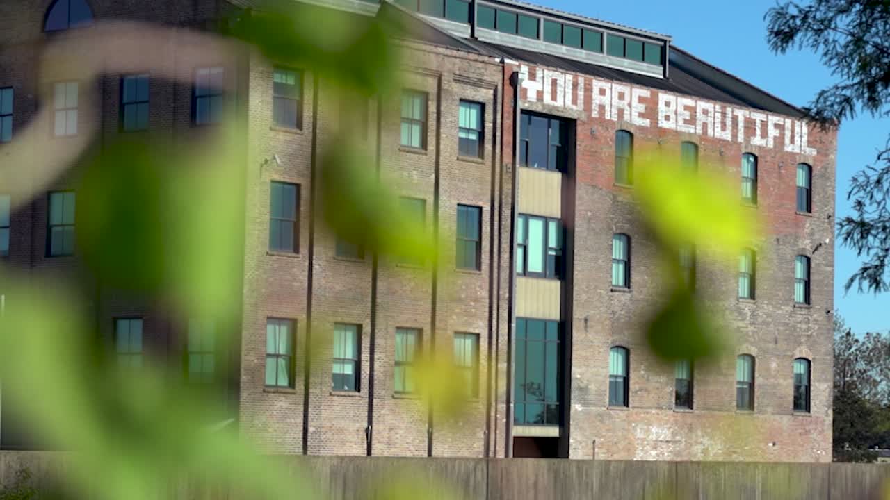 Inspiring mural You Are Beautiful on brick building with foreground plants