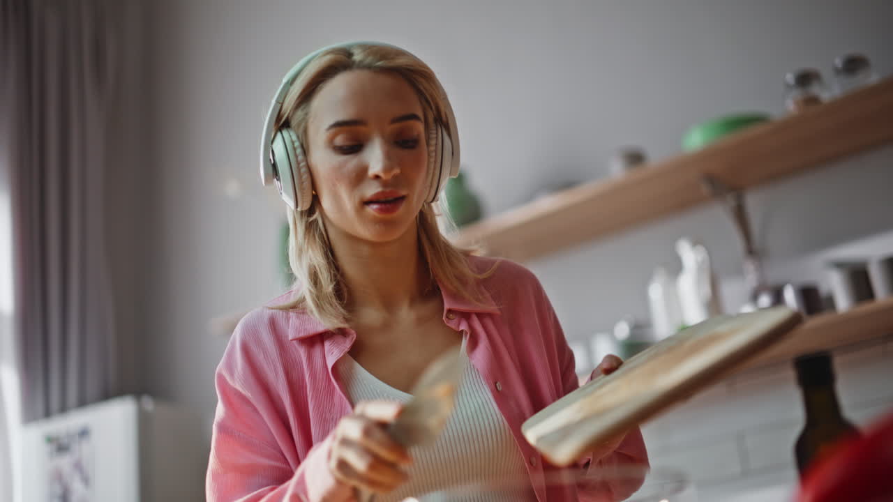 Chef hands slicing pepper on wooden board kitchen closeup. Girl listening music