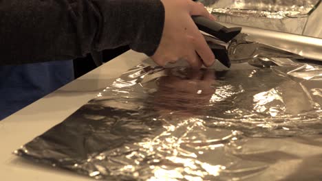 a girl cuts aluminum foil as prep for baking some millionaire shortbread cookies