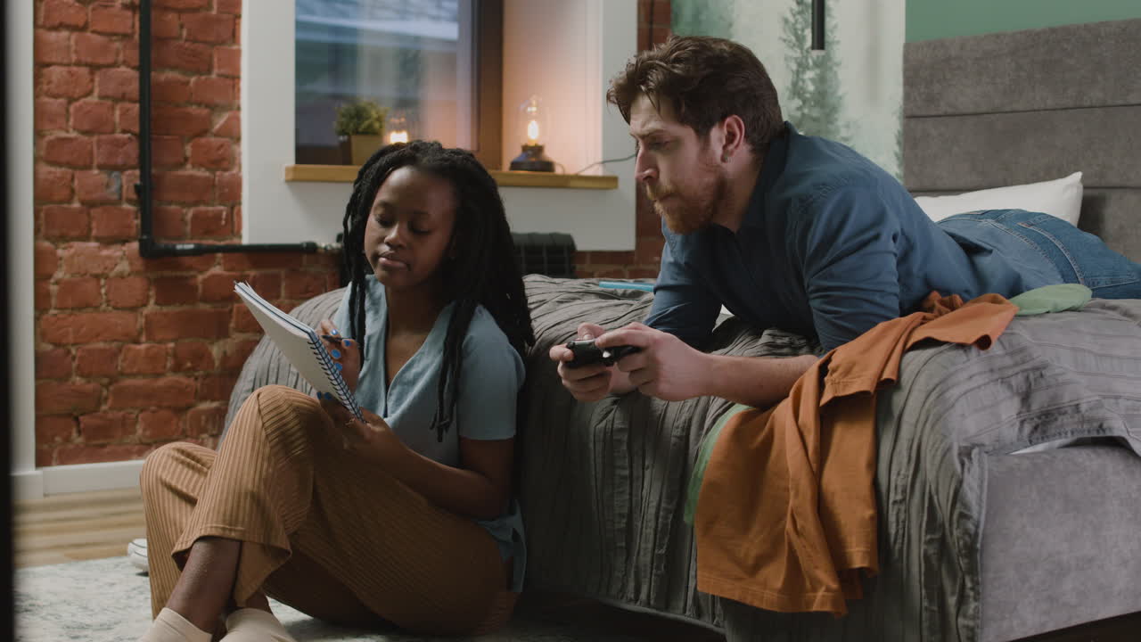 Girl Are Taking Notes Lying In Bedroom While Her Male Roommate Are Playing Video Games