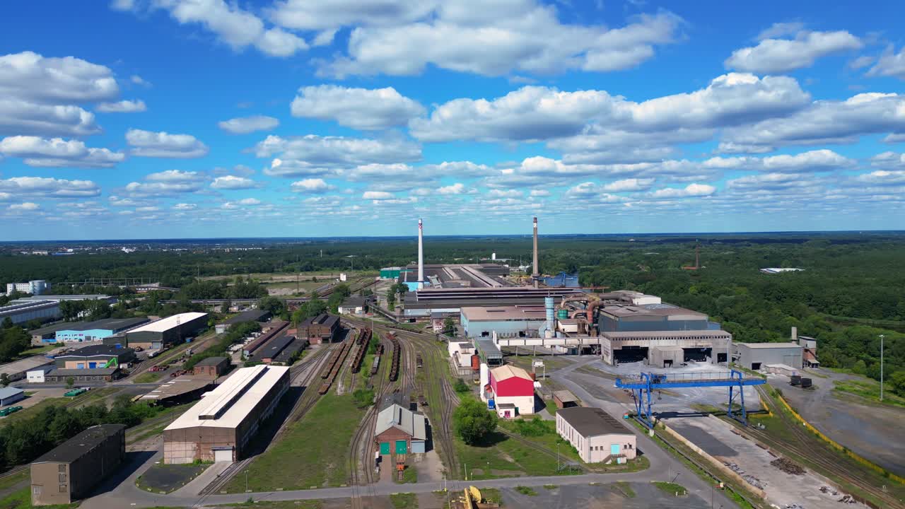Hennigsdorf electric steel factory with train tracks, chimneys, and industrial buildings under a blue sky. Unique aerial view flight panorama orbit drone