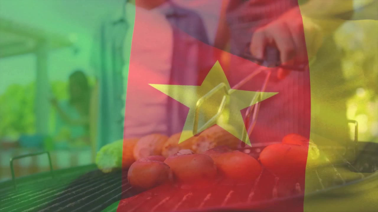 Người đàn ông mặc tạp dề sọc đặt cà chua lên vỉ nướng, lật bằng kẹp để đảm bảo chín đều.