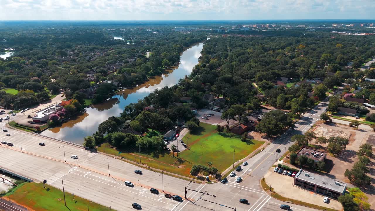 An aerial shot a brown river, surrounded by trees in a suburban neighborhood, on a partly cloudy day, recorded at 60 frames per second.