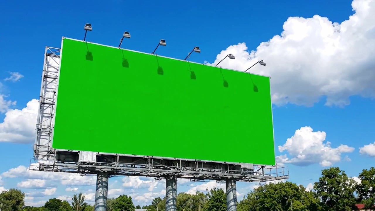 Tomt grønt billboard mod en klar blå himmel med bløde skyer, der fremhæver plads til reklame og promovering i et klart bylandskab