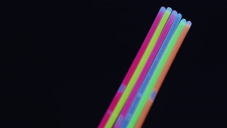 animation of colorful neon glow sticks over black background with copy space