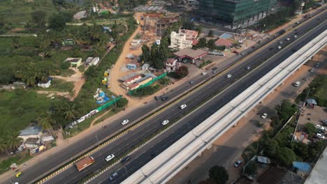 an aerial view of an indian highway that is expanding quickly, with a service road, fast-moving automobiles, and a metro train bridge under construction