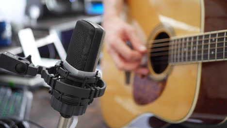 a studio musician playing an acoustic guitar and recording audio into a condenser microphone