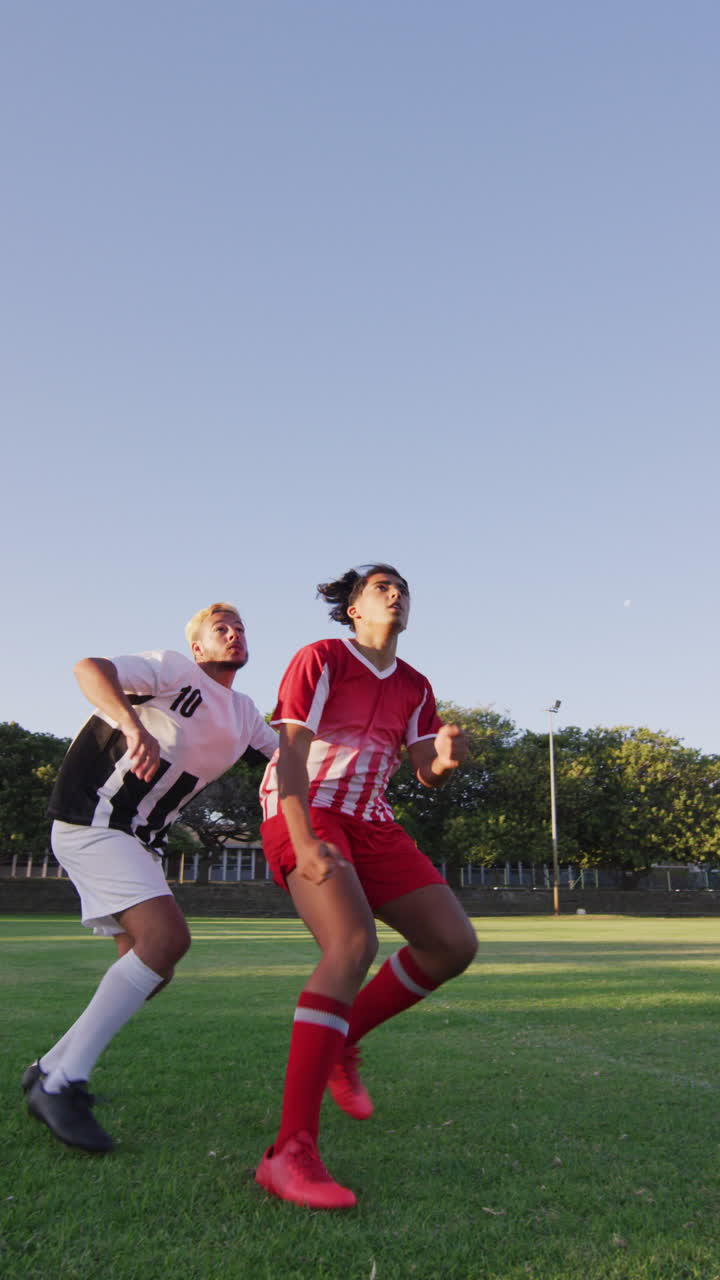 Vertical video of diverse male soccer players training outside, kicking ball