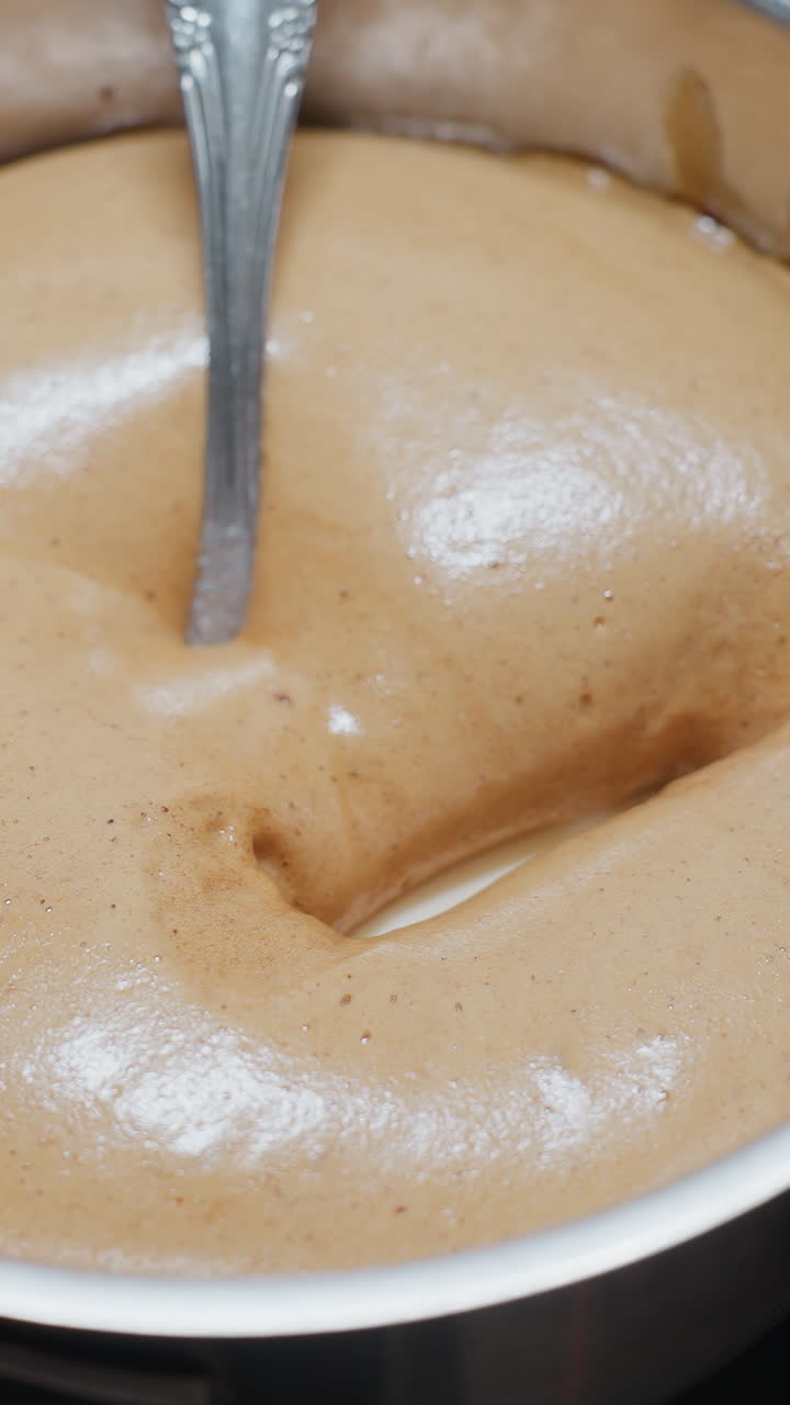 Close-up of white substance inside swollen pap with spoon submerged in pot, thick, bubbly texture forming on surface as it cooks on stovetop, showing creamy consistency and rich color