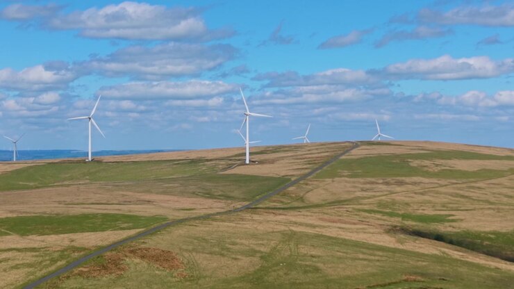 Lang landevei på en ås med roterende vindturbiner over et walisisk landskap. Droneklipp av infrastruktur for fornybar energiproduksjon i Storbritannia.