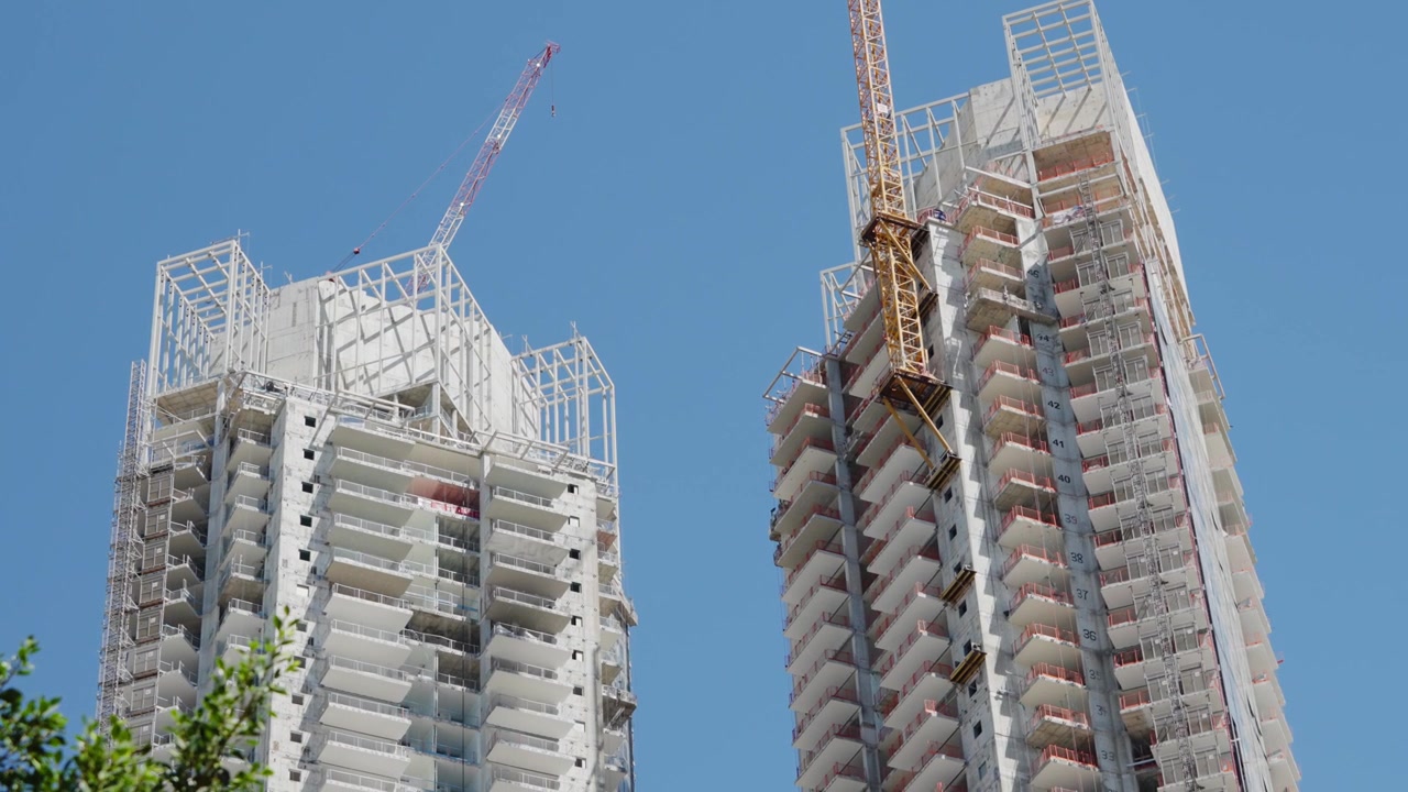 Vista en ángulo contrapicado de dos torres residenciales de gran altura en construcción con grúas contra un cielo azul despejado en Tel Aviv, Israel, que muestra el desarrollo urbano moderno y el crecimiento inmobiliario