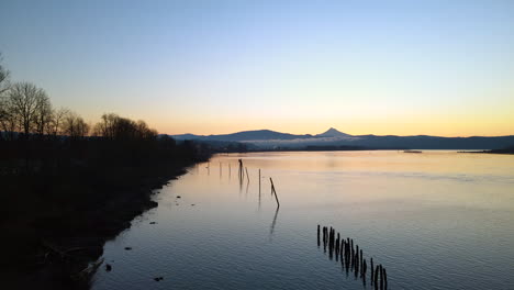 drone flying low above a large lake during sunrise, trees and mountains on the coast and shore