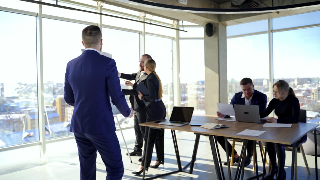 Portrait of businessman in suit in busy office. Successful man in elegant suit speaking about his work on the background of young office workers indoors.