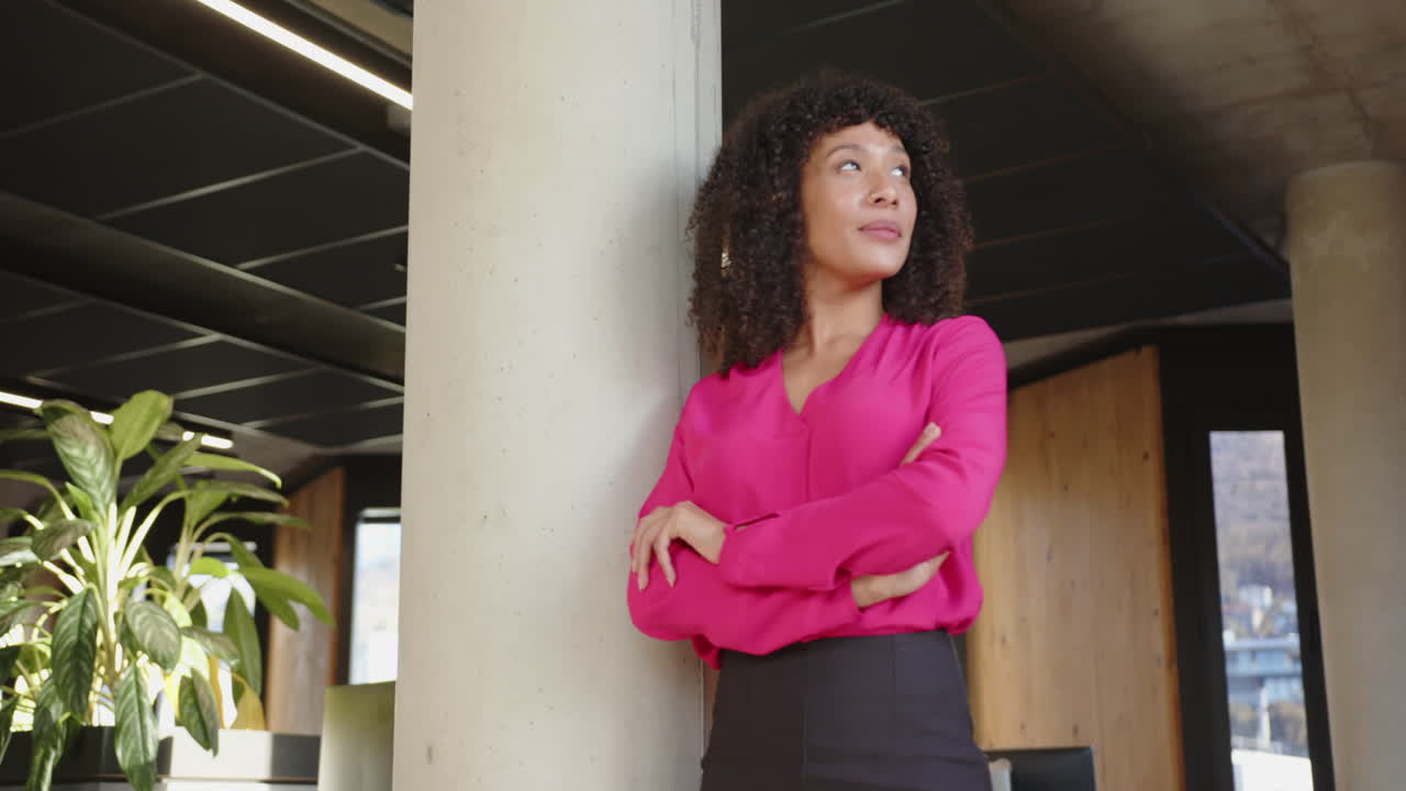 Confident businesswoman in pink blouse standing with arms crossed in office