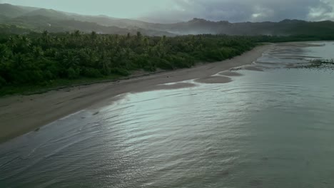 Beach-and-hilly-forest-landscape-in-cloudy-Philippines,-forward-aerial