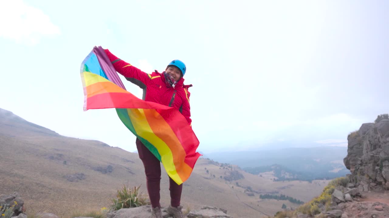 mujer joven con la bandera del arco iris lgbt en las montañas